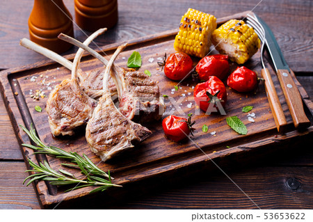 Lamb ribs grilled on cutting board with roasted vegetables. Lamb ribs grilled on cutting board with roasted vegetables. 53653622