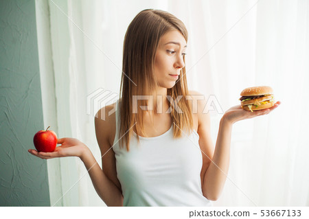Dieting concept, beautiful young woman choosing between healthy food and junk food 53667133