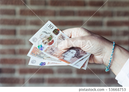 Woman holding pounds sterlings against brick wall background Woman holding pounds sterlings against brick wall background 53668753