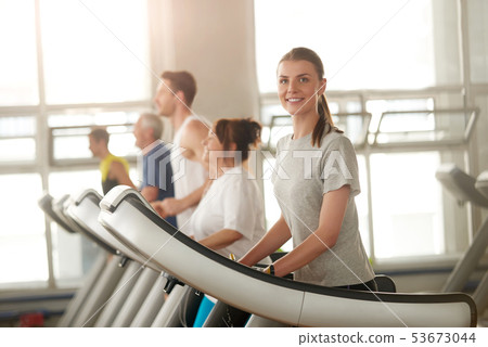 Fit woman running on treadmill smiling at camera. 53673044