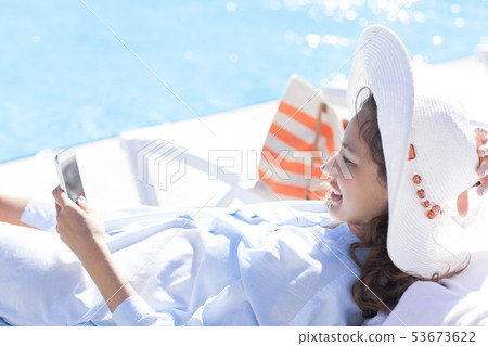 Woman using mobile phone by the pool Woman using mobile phone by the pool 53673622