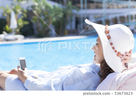 Woman using mobile phone by the pool Woman using mobile phone by the pool 53673623