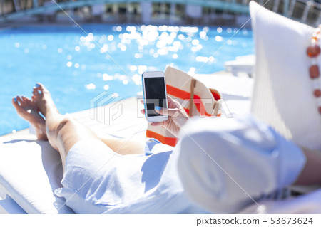 Woman using mobile phone by the pool Woman using mobile phone by the pool 53673624