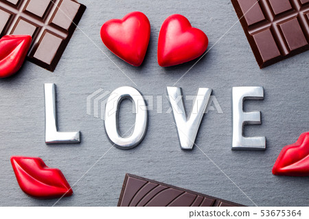 Love word, heart and lips shaped chocolate candies with chocolate bars on slate background. 53675364