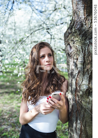 Young woman a smart phone under the blooming Young woman a smart phone under the blooming 53676048