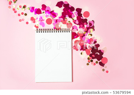 Holiday decorations with notebook on pastel pink background with red pink white and gold confetti. 53679594