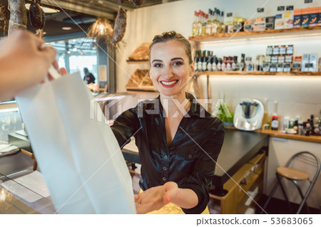 Shop assistant handing over bag with groceries to customer Shop assistant handing over bag with groceries to customer 53683065