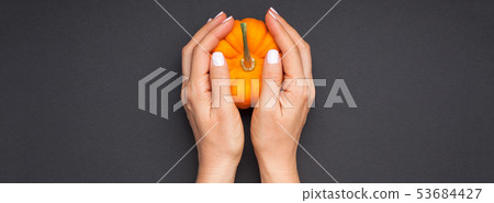 Small orange pumpkin woman hands black background Small orange pumpkin woman hands black background 53684427