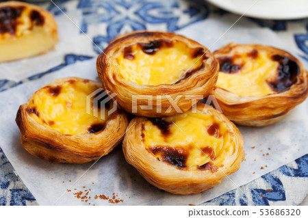 Egg tart, traditional Portuguese dessert, pastel de nata on a plate. Blue textile background. Egg tart, traditional Portuguese dessert, pastel de nata on a plate. Blue textile background. 53686320
