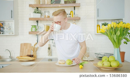 Blonde man is drinking coffee while having breakfast at the kitchen 53686380