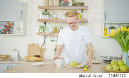 Beautiful blonde man is making breakfast for his girlfriend in the morning at the kitchen 53686382