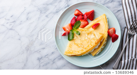 Crepes, thin pancakes with cream cheese, strawberries. Marble background. Top view. Copy space. 53689346