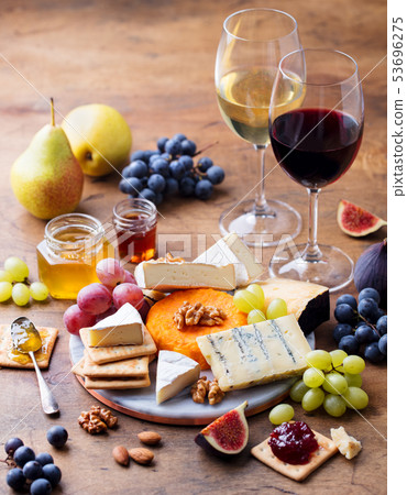 Grape, cheese, figs and honey with a glasses of red and white wine on a wooden background. Grape, cheese, figs and honey with a glasses of red and white wine on a wooden background. 53696275