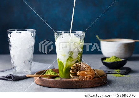 Matcha, green tea ice tea pouring in tall glass on wooden plate. Grey stone background. Matcha, green tea ice tea pouring in tall glass on wooden plate. Grey stone background. 53696376
