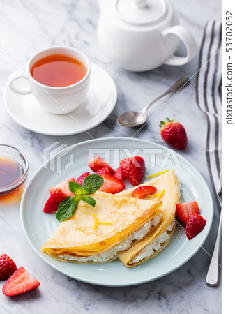 Crepes, thin pancakes with fresh strawberry and ricotta with cup of tea. Marble background. Crepes, thin pancakes with fresh strawberry and ricotta with cup of tea. Marble background. 53702032