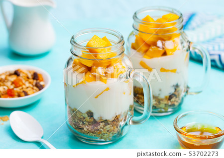 Fresh mango fruit with yogurt and granola in jars. Blue stone background. Close up. Fresh mango fruit with yogurt and granola in jars. Blue stone background. Close up. 53702273