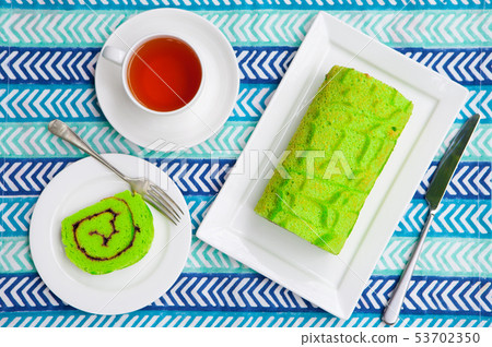 Green roll cake with a cup of tea on blue textile background. Top view. 53702350