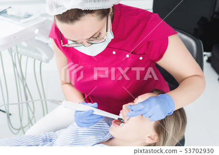 Close-up A professional dentist woman in glasses and overalls examines the oral cavity of a young Close-up A professional dentist woman in glasses and overalls examines the oral cavity of a young 53702930