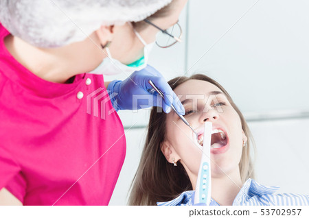 Close-up A professional dentist woman in glasses and overalls examines the oral cavity of a young 53702957