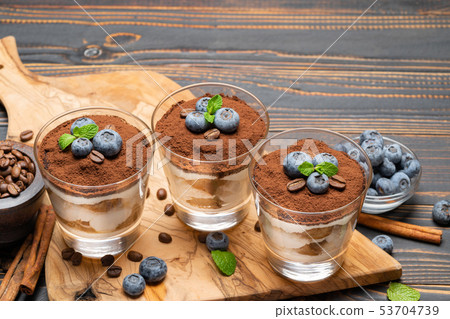 Classic tiramisu dessert in a glass with blueberries on wooden background Classic tiramisu dessert in a glass with blueberries on wooden background 53704739