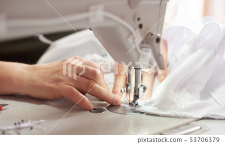 Female hands at sewing process and repairing white fabric on professional manufacturing machine 53706379