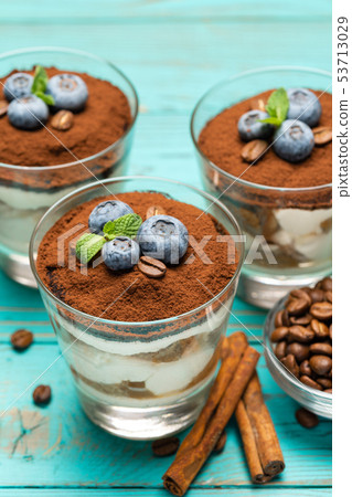 Classic tiramisu dessert in a glass with blueberries on blue wooden background Classic tiramisu dessert in a glass with blueberries on blue wooden background 53713029
