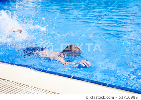 boy in swimming trunks swims in the blue water pool on summer vacation. 53716989