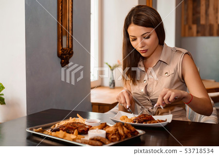Beautiful girl eats chicken leg with with knife and fork Beautiful girl eats chicken leg with with knife and fork 53718534