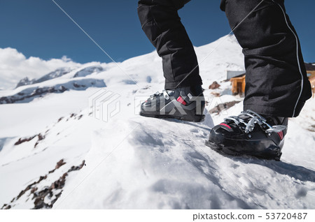 A close-up of a skier's leg in ski boots without skis stands on a knoll of bliss against the 53720487