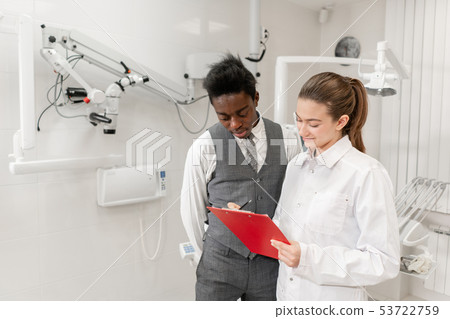 African male patient in dental clinic. Young Woman dentist makes a diagnosis and records African male patient in dental clinic. Young Woman dentist makes a diagnosis and records 53722759