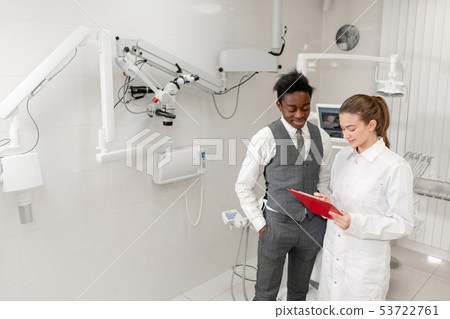 Young Woman dentist makes a diagnosis and records recommendations. African male patient in dental 53722761