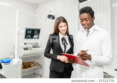 Woman patient at dental clinic. Young African male dentist makes a diagnosis and records Woman patient at dental clinic. Young African male dentist makes a diagnosis and records 53722778