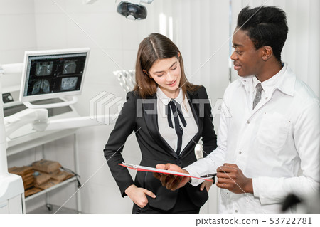 Woman patient at dental clinic. Young African male dentist makes a diagnosis and records Woman patient at dental clinic. Young African male dentist makes a diagnosis and records 53722781