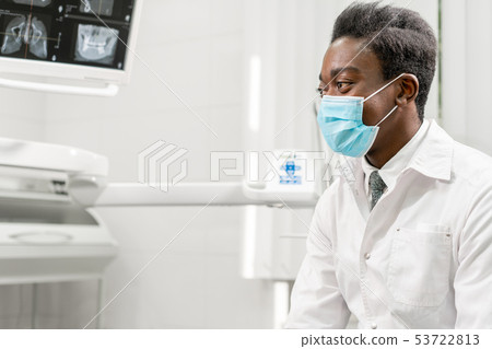 Young African male dentist shows x-rays on the monitor. Medicine, health, stomatology concept Young African male dentist shows x-rays on the monitor. Medicine, health, stomatology concept 53722813