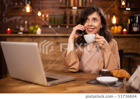 Attracive young business woman drinking coffee and having a phone call in a modern coffee shop Attracive young business woman drinking coffee and having a phone call in a modern coffee shop 53736604