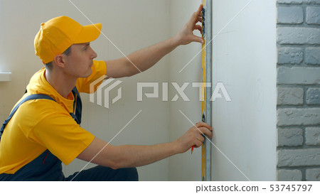 Repairman making measurement of wall. 53745797