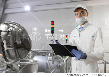 Inspector in a mask and a scrub stands with a folder-tablet in his hands at the dairy plant 53748257
