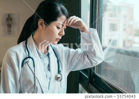 Depressed doctor leaning against window upset 53754043