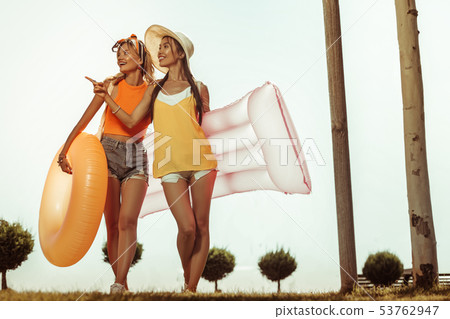 Cheerful ladies heading to the beach with inflatable water toys. Cheerful ladies heading to the beach with inflatable water toys. 53762947