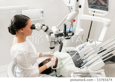 Modern equipment microscope in dental office. Young woman dentist treating root canals. Man patient 53765874