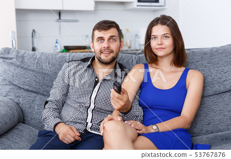 Smiling young couple sitting on sofa at home watching TV Smiling young couple sitting on sofa at home watching TV 53767876