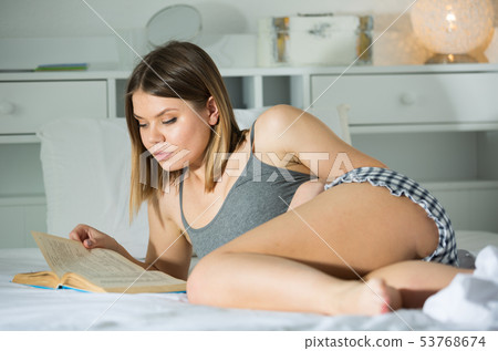 Smiling young woman is relaxing in bed and reading book on bed 53768674