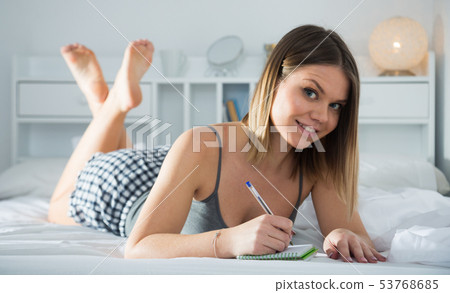 Young woman is relaxing in bed and making schedule on bed Young woman is relaxing in bed and making schedule on bed 53768685