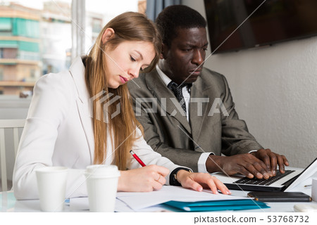 Male and female colleagues working with laptop and documents at table 53768732
