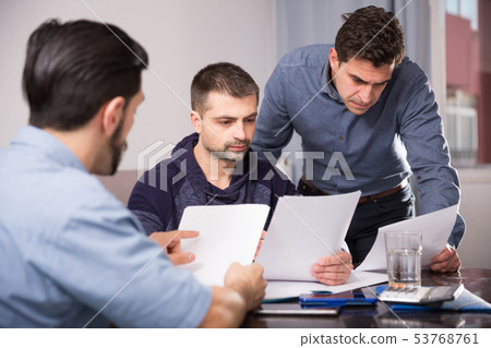 Three upset males with papers at table Three upset males with papers at table 53768761