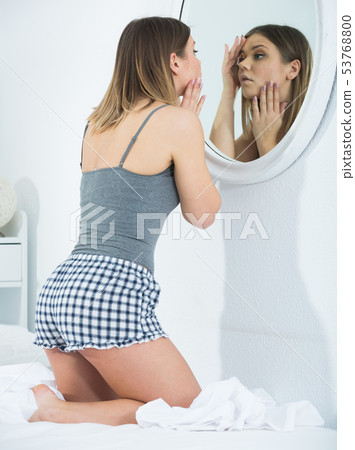 Girl touching face and looking at mirror in bedroom in morning 53768800
