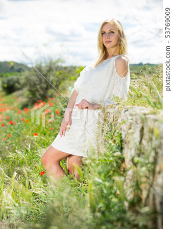 Woman wearing white dress posing near fields with wild flowers 53769009