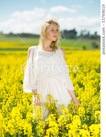 Young woman in yellow oilseed rape field posing in white dress Young woman in yellow oilseed rape field posing in white dress 53769019