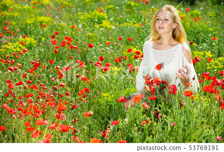 Woman wearing white dress in poppy field and enjoying summer day 53769191