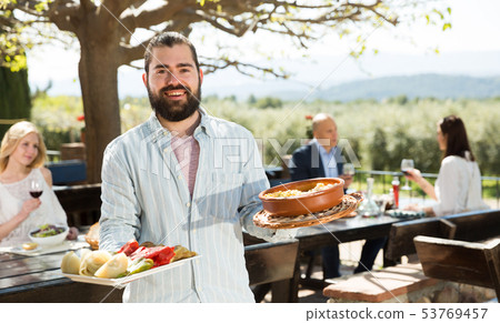 Bearded waiter inviting on outdoor terrace Bearded waiter inviting on outdoor terrace 53769457